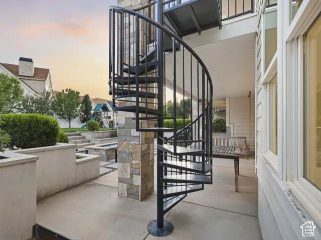 Black metal spiral staircase with stone veneer column, concrete patio, and built-in planters