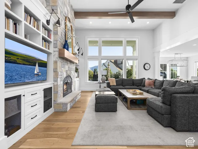 Vaulted ceiling with exposed beam, stone-faced fireplace, built-in shelving, large multi-pane windows, and wood-finish flooring