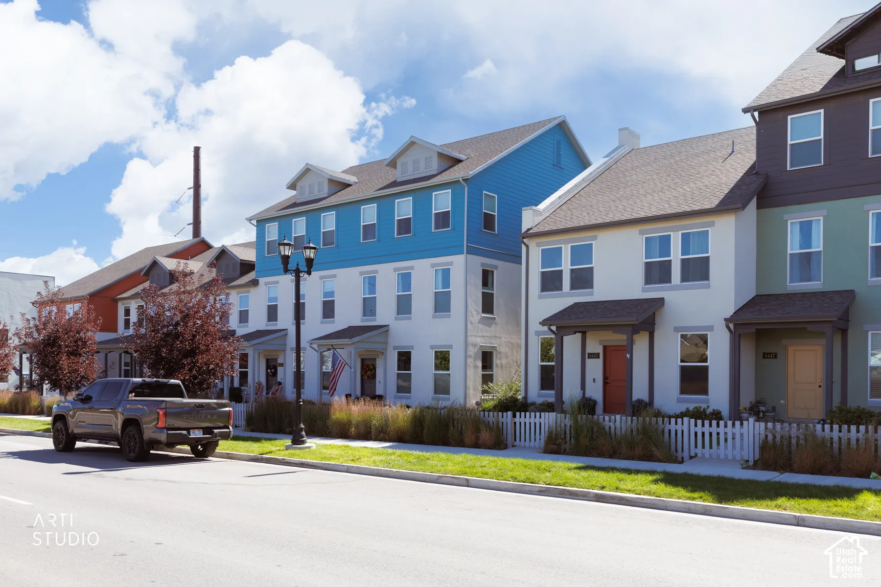 Multi-story townhome featuring a neutral stucco exterior, covered entry, and traditional white picket fence