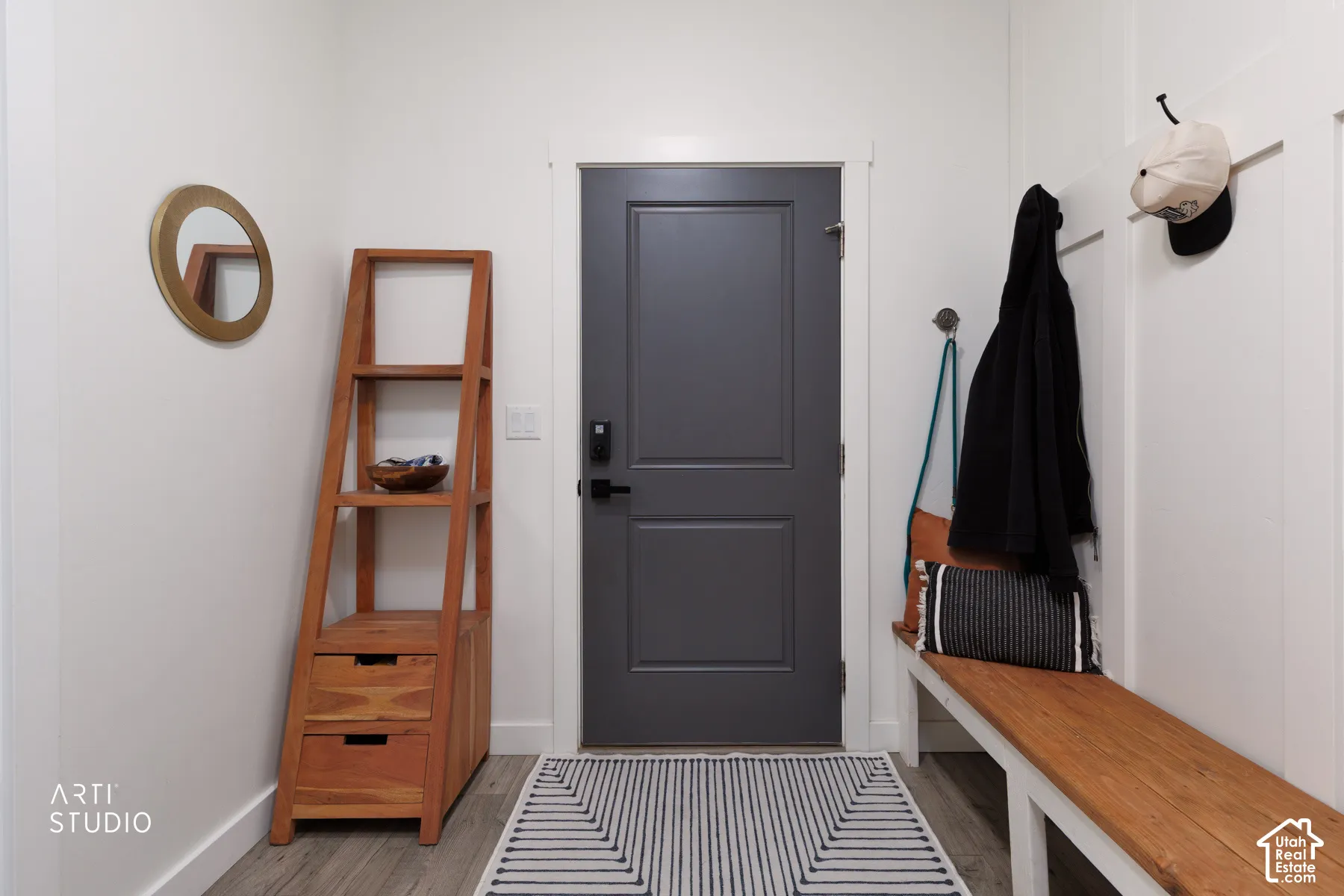 Entryway featuring a dark paneled door with smart lock hardware, wood-finish flooring, a built-in wooden bench, and white paneled wall accents