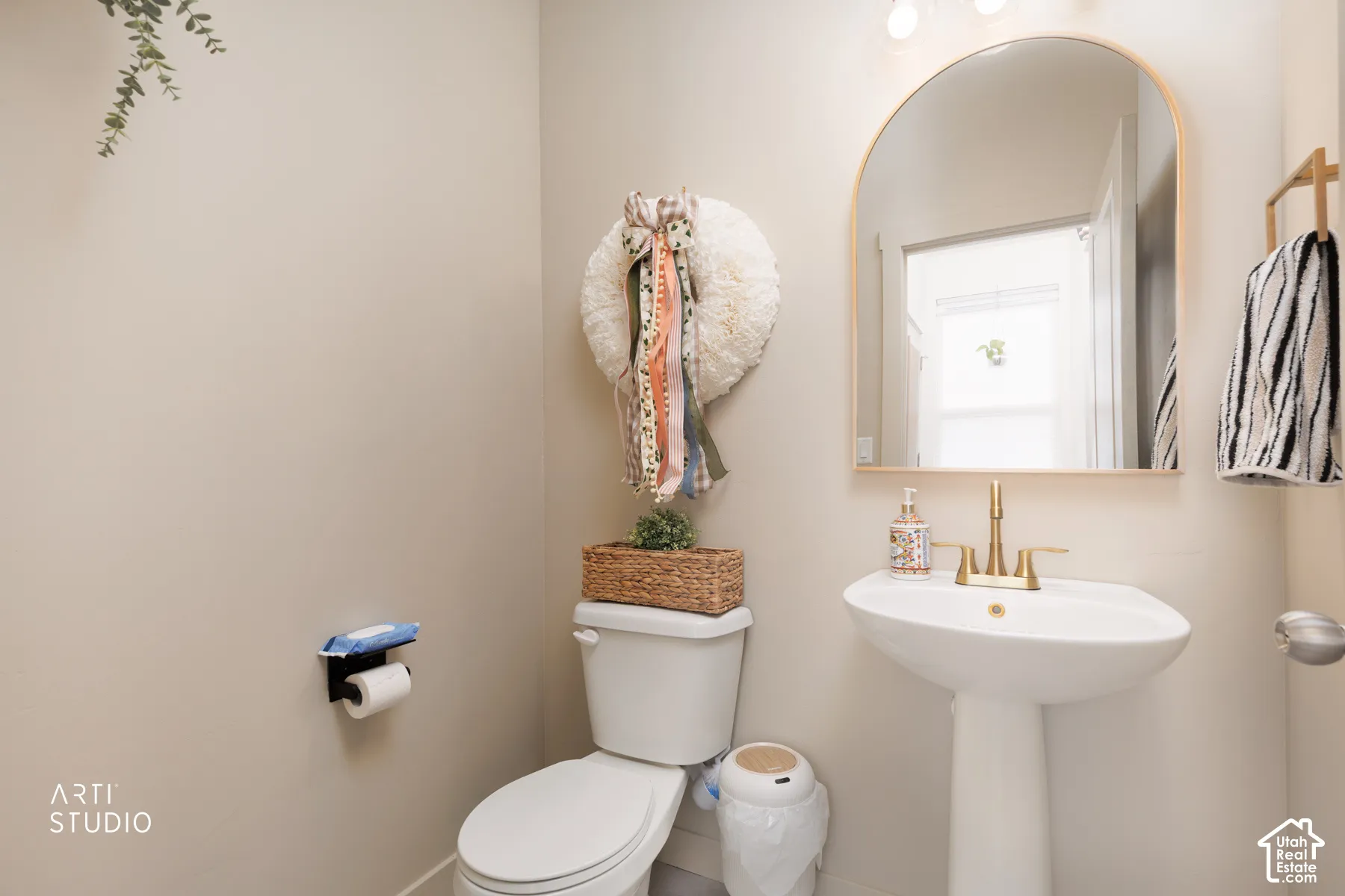 Pedestal sink with brass-finish faucet, arched mirror, and wall-mounted lighting