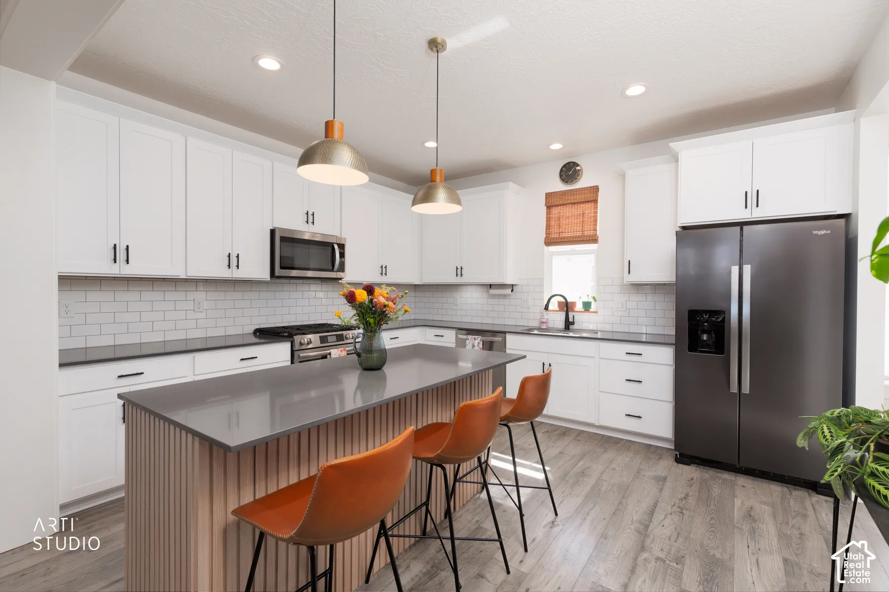 White cabinetry with black hardware, subway tile backsplash, stainless steel appliances, central island with slat wood-finish paneling, and wood-finish flooring