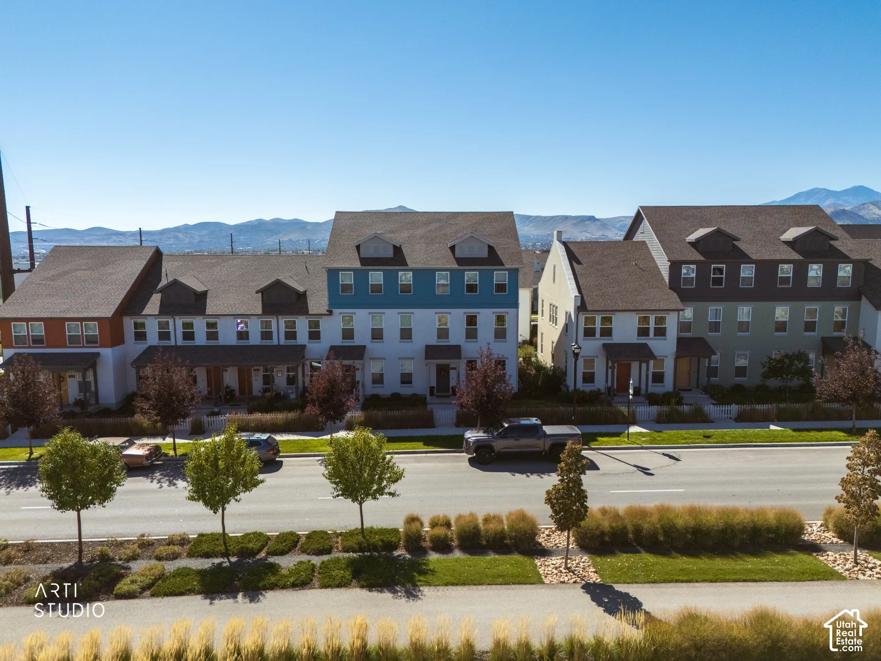 Row of multi-story townhomes with dormer windows, individual front porches, and varied exterior siding colors