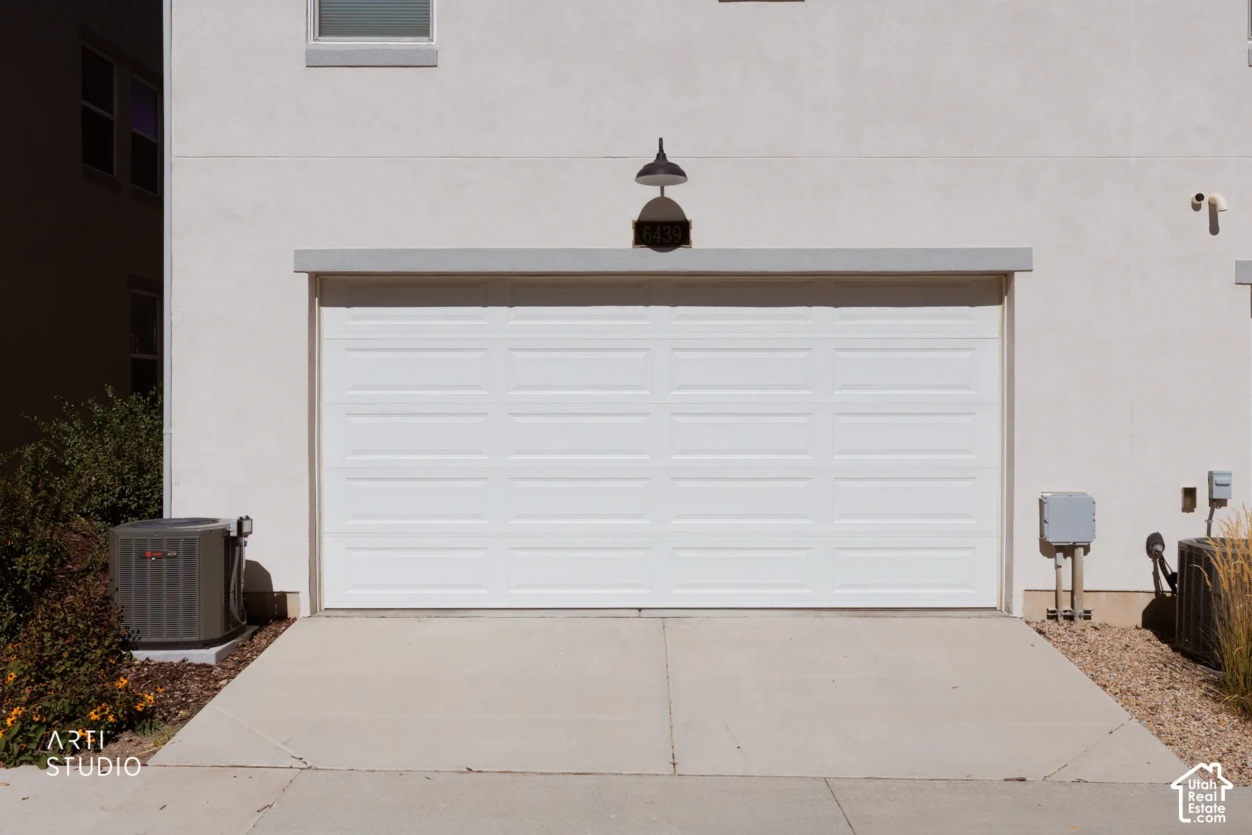 White paneled garage door with an overhead gooseneck light fixture, concrete driveway, and stucco exterior