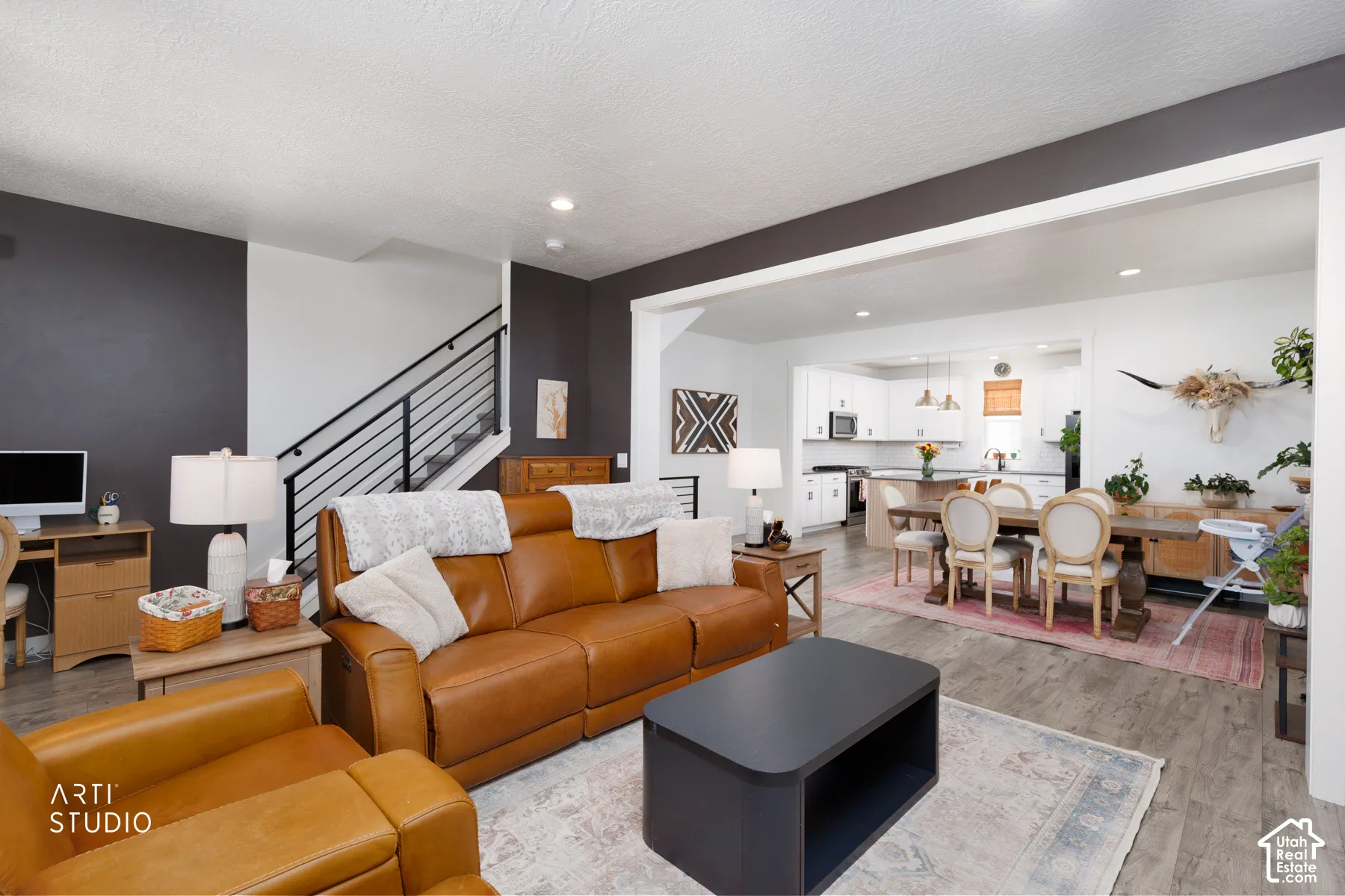Open-concept living space featuring wood-finish flooring, recessed lighting, and a modern staircase with black metal railings