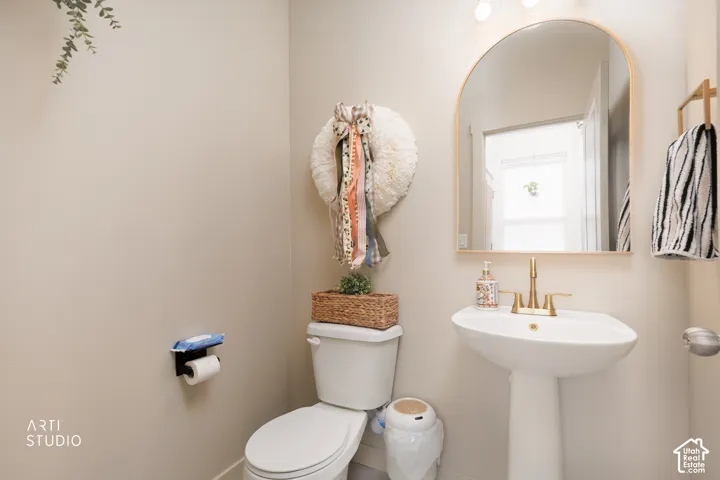 Pedestal sink with brass-finish faucet, arched mirror, and wall-mounted lighting