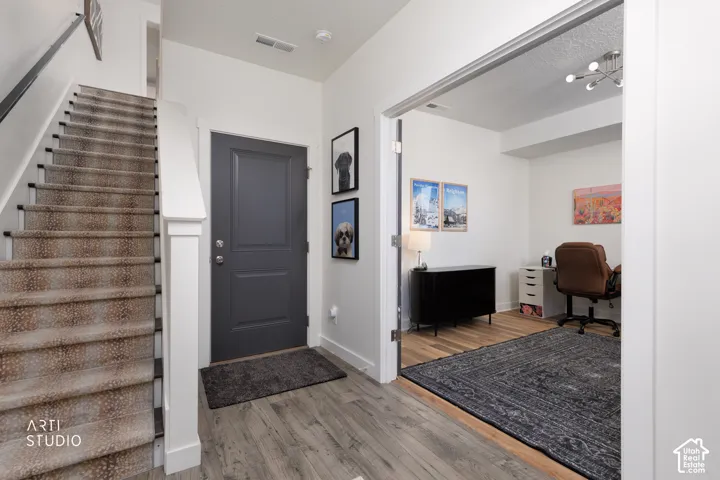 Wood-finish flooring, staircase with patterned carpet, and a dedicated room with a modern light fixture