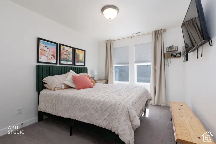 Plush carpet flooring, dual windows with blinds and drapes, wall-mounted television, and a semi-flush mount ceiling light