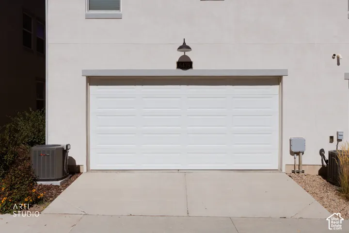 White paneled garage door with an overhead gooseneck light fixture, concrete driveway, and stucco exterior