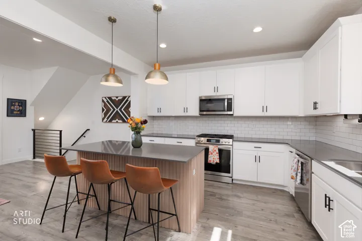 Kitchen featuring white cabinetry, subway tile backsplash, stainless steel appliances, and wood-finish flooring