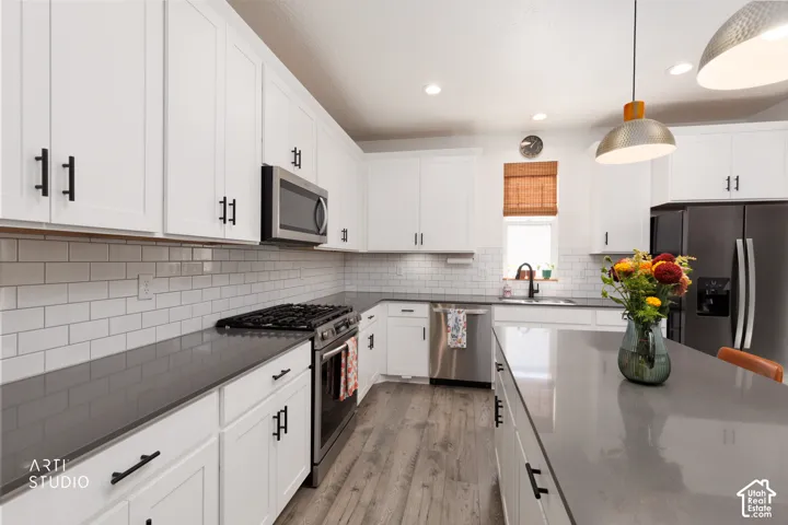 White shaker cabinetry, dark countertops, subway tile backsplash, stainless steel appliances, and wood-finish flooring