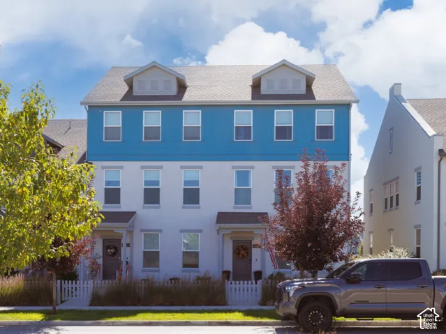Three-story townhome featuring blue siding, white exterior walls, multiple windows, and a white picket fence