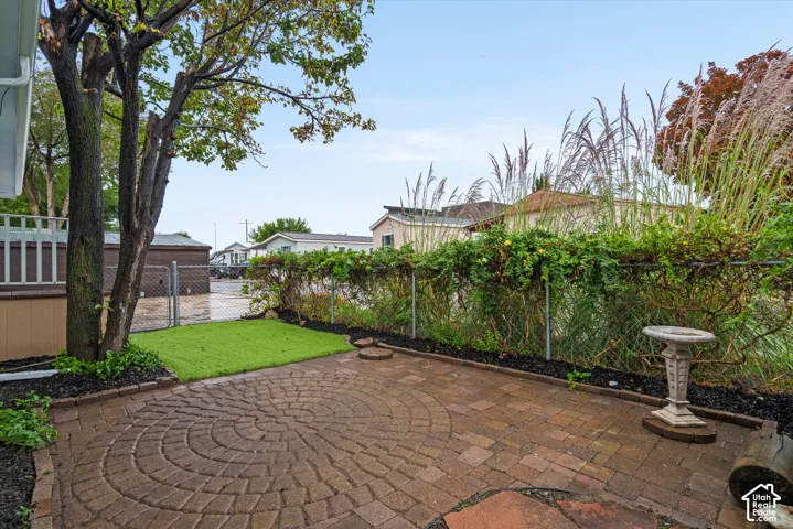 Expansive paver patio with a circular pattern, artificial turf accent, mature tree, and garden beds