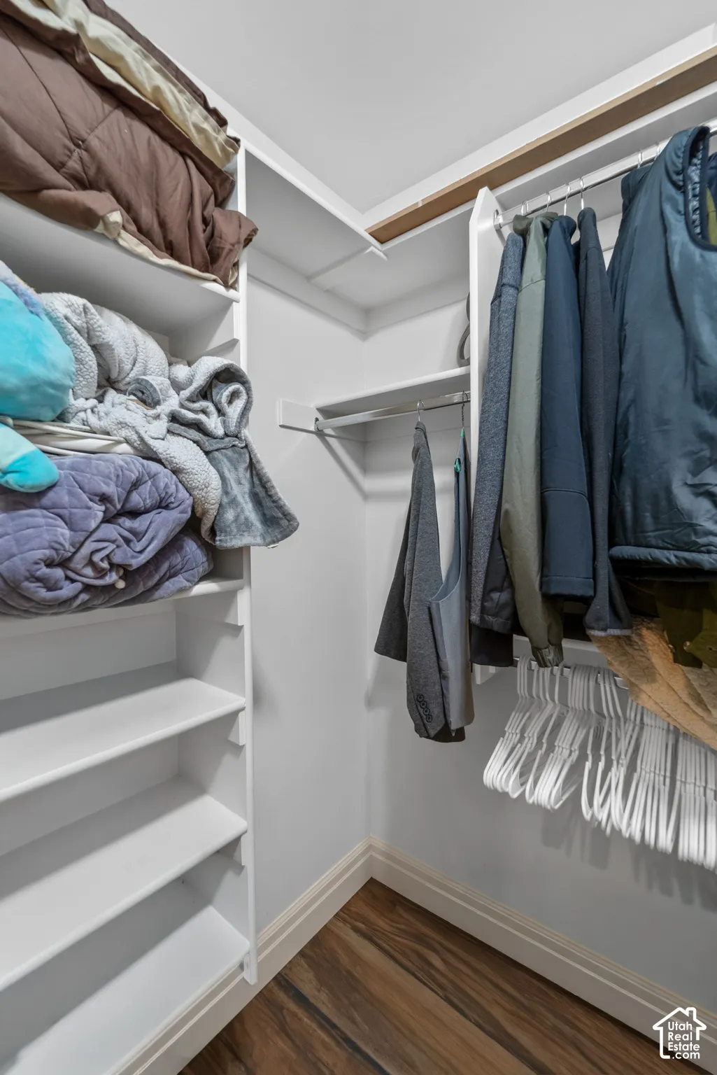 Walk-in closet featuring built-in shelving, two hanging rods, and wood-finish flooring