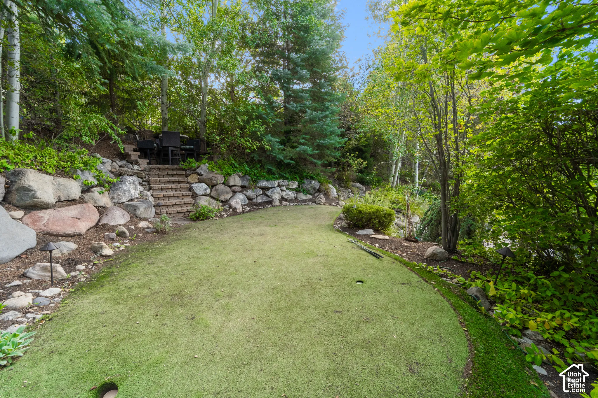 Putting green with a gentle curve, brick steps, and a stone retaining wall.
