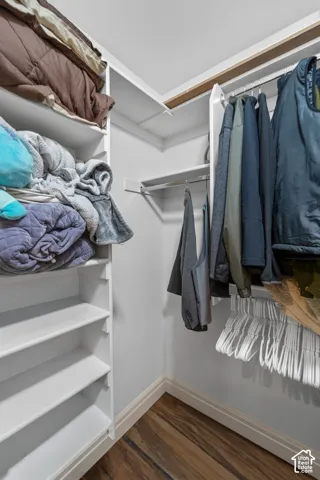 Walk-in closet featuring built-in shelving, two hanging rods, and wood-finish flooring