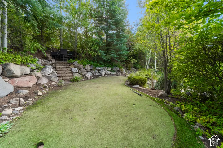 Putting green with a gentle curve, brick steps, and a stone retaining wall.