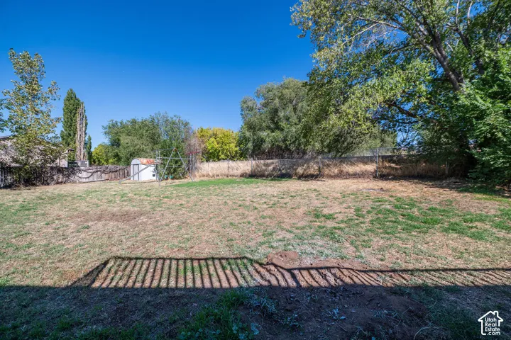 Expansive backyard featuring a storage shed, mature trees, and perimeter fencing
