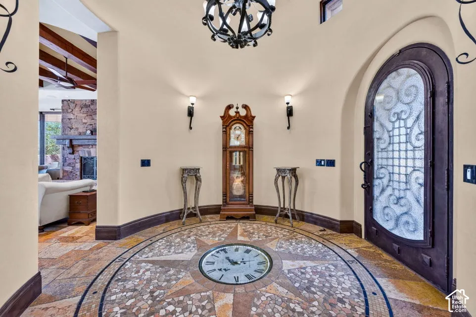 Arched entry door with decorative ironwork, custom tile mosaic flooring, and vaulted ceiling with exposed wood beams