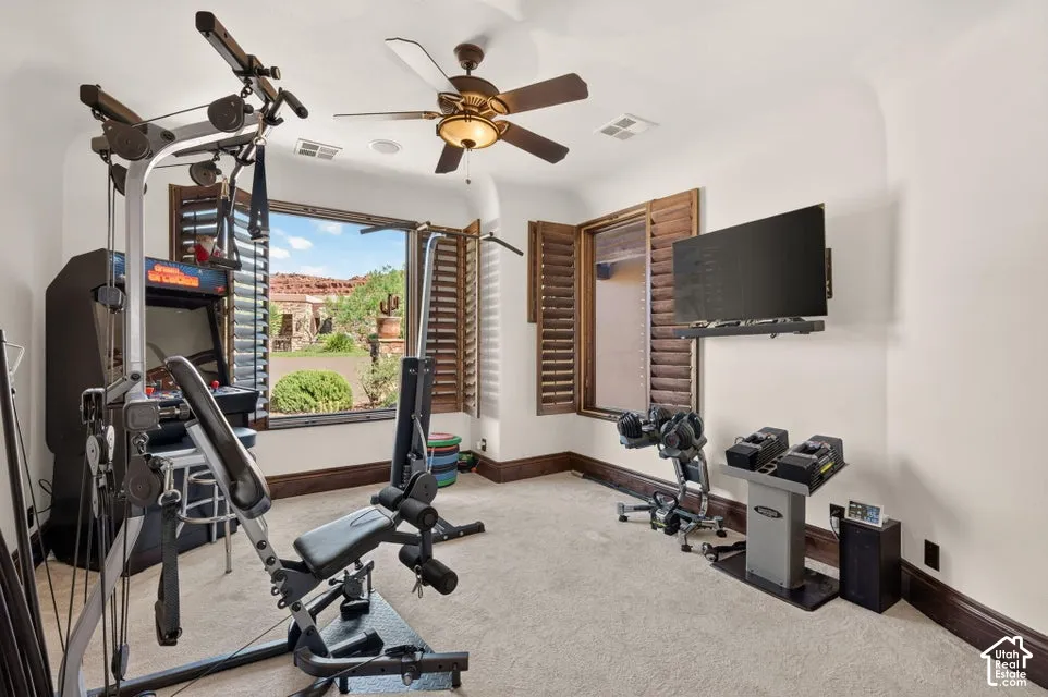 Carpeted room featuring a ceiling fan, wall-mounted television, and large windows with plantation shutters