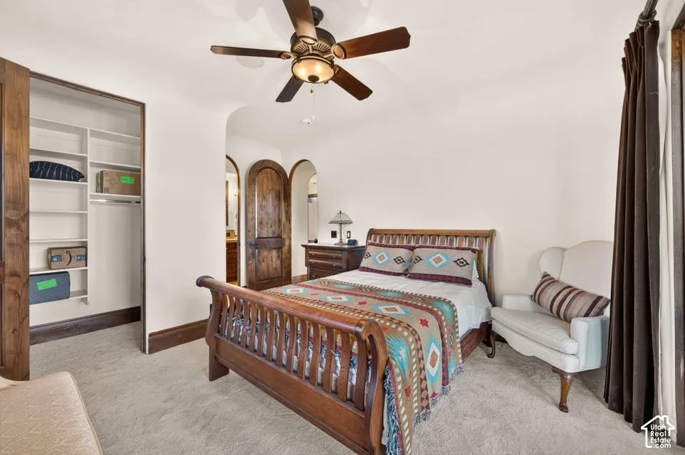 Carpeted bedroom featuring a ceiling fan, a custom built-in closet, and arched doorways with wood panel doors