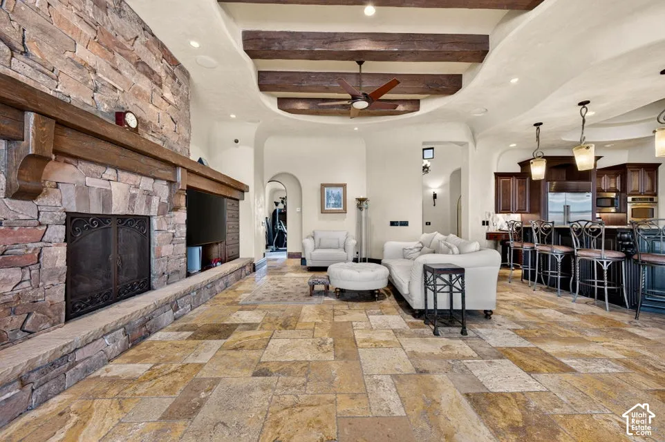 Stone-clad fireplace with a wood mantle, wood-beamed ceiling, textured tile flooring, recessed lighting, and a built-in kitchen island