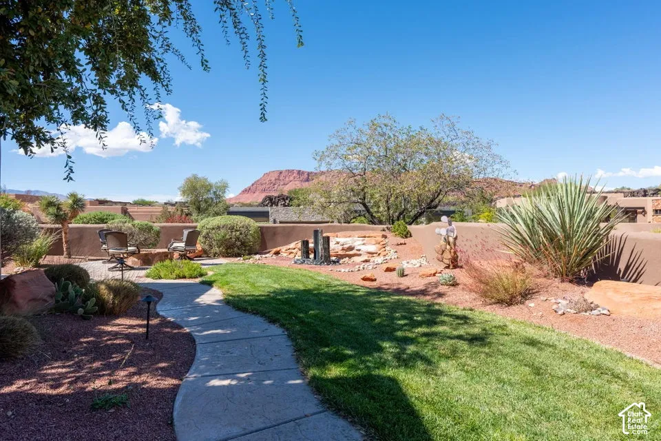 Landscaped yard featuring a winding paved path, green lawn, rock garden elements, and desert plantings