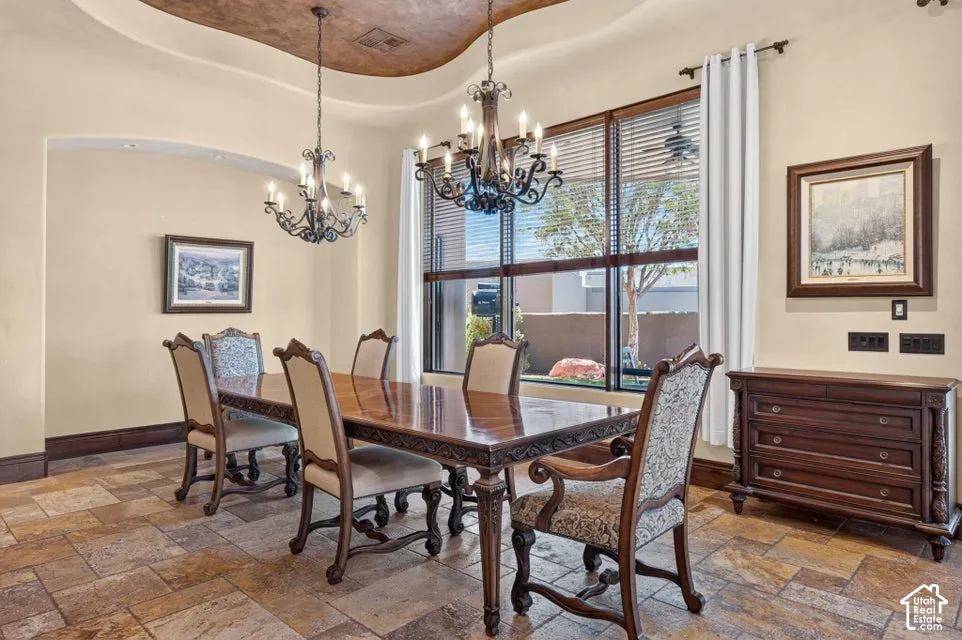 Tray ceiling with textured finish, two ornate chandeliers, and large window with blinds and drapes