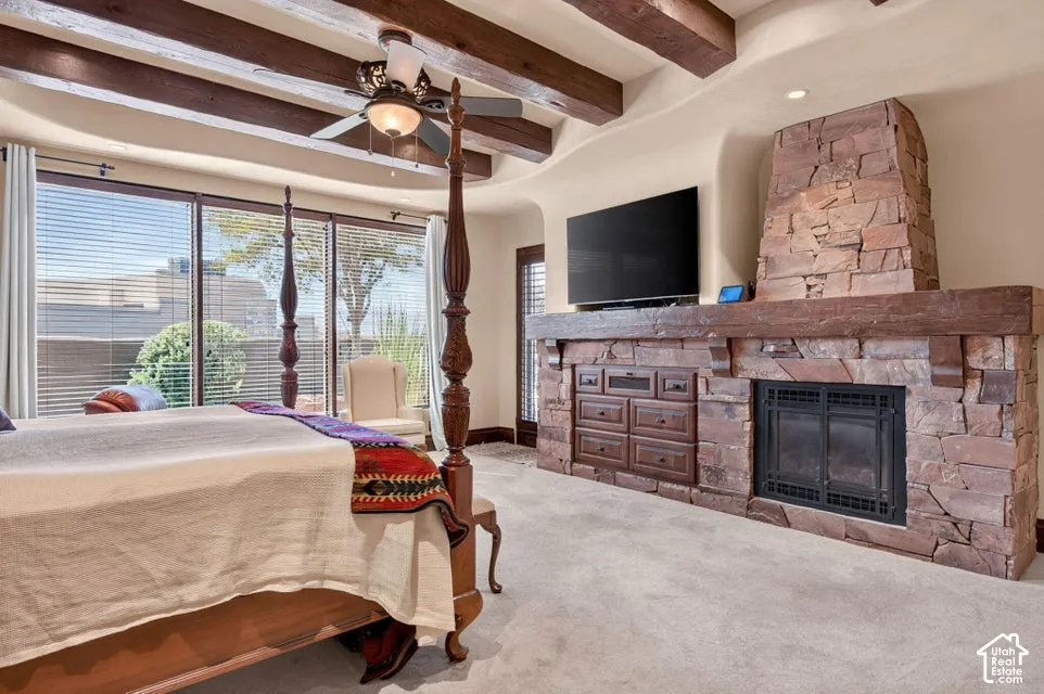 Exposed wood beams, stone-clad fireplace with wood mantel, built-in cabinetry, ceiling fan, and large windows with blinds