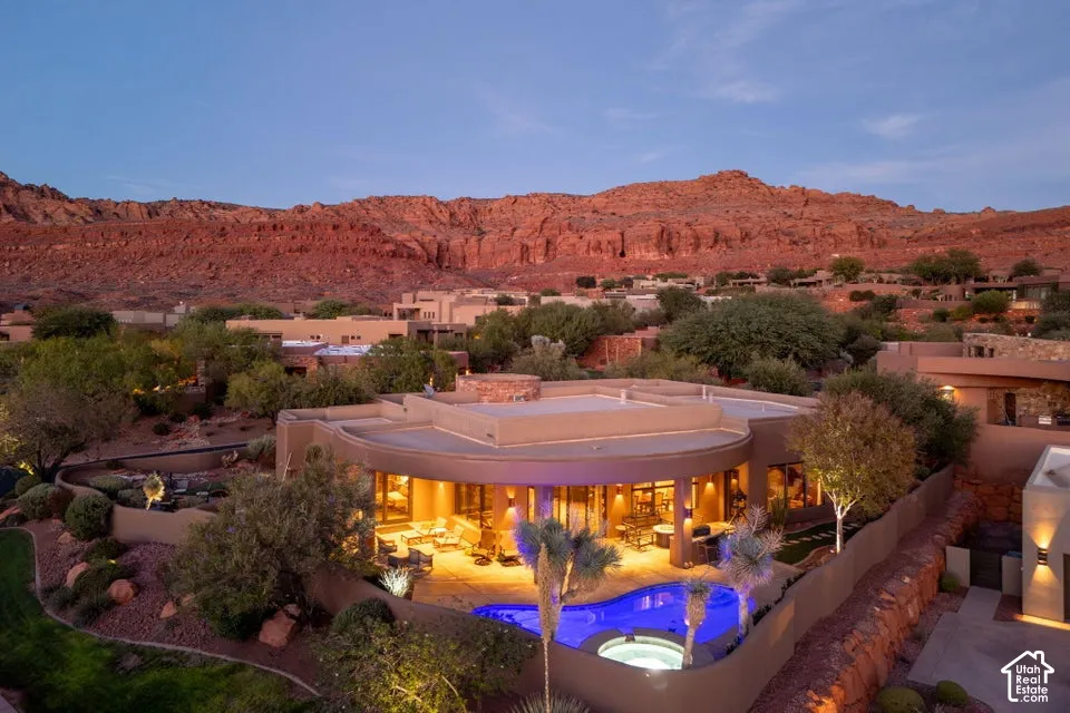 Curved stucco exterior with an integrated swimming pool, spa, and illuminated patio space