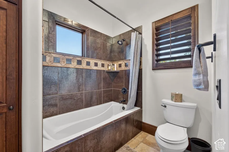 Bathtub with dark tile surround, accent tile band, and built-in shower niche