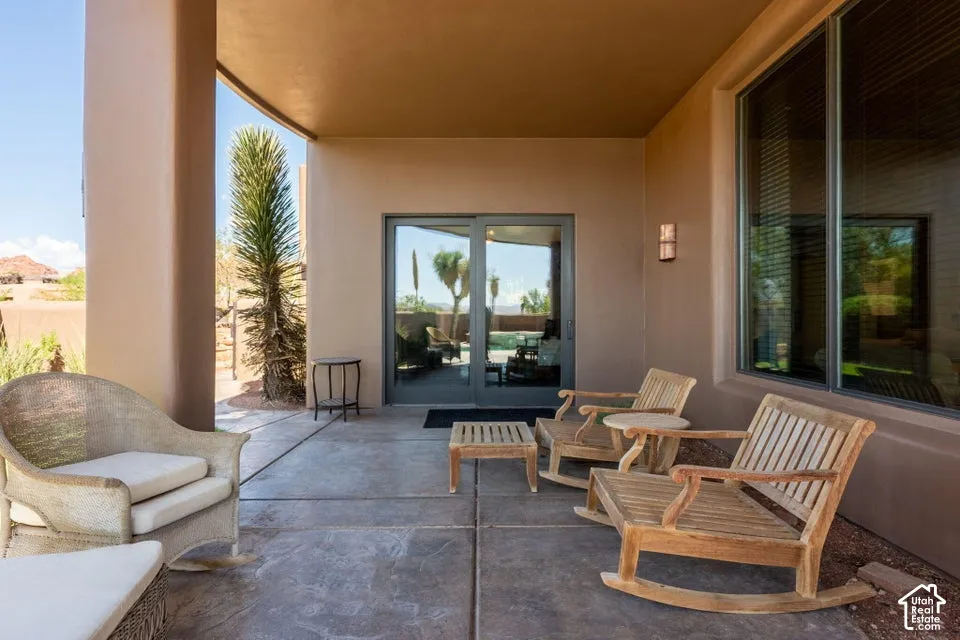 Covered patio with stamped concrete flooring, multi-panel sliding glass door, fixed windows, and exterior wall sconce