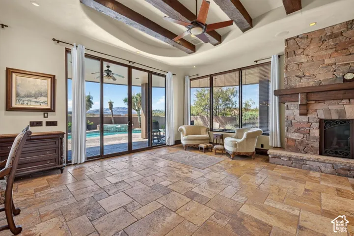 Expansive great room showcasing soaring ceilings with exposed wood beams, extensive multi-panel sliding glass doors opening to outdoor living spaces, and a substantial wood-finish tile floor
