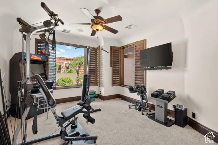 Carpeted room featuring a ceiling fan, wall-mounted television, and large windows with plantation shutters