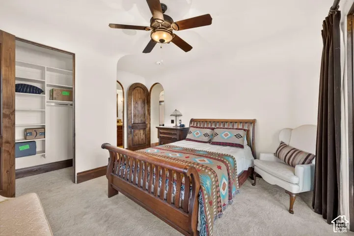 Carpeted bedroom featuring a ceiling fan, a custom built-in closet, and arched doorways with wood panel doors