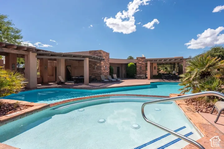Resort-style pool area featuring an integrated spa, extensive hardscaping, stone-clad architectural elements, and covered patio areas