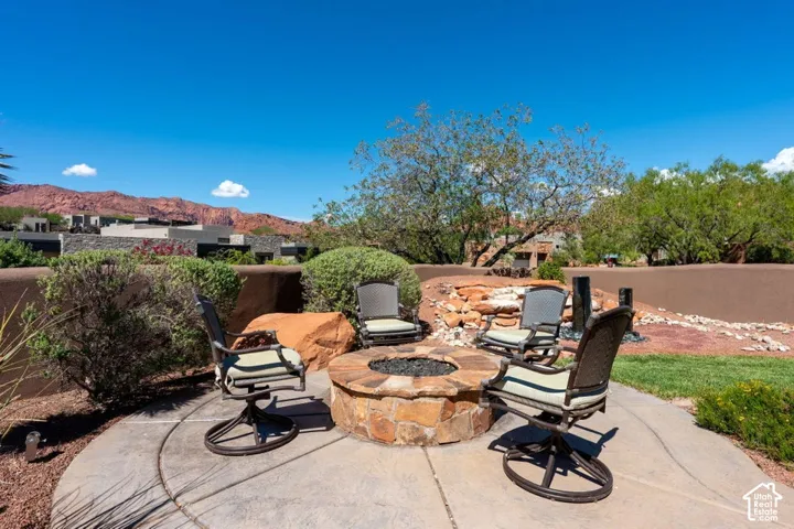 Circular concrete patio with a built-in stone fire pit, surrounded by desert landscaping and mature trees