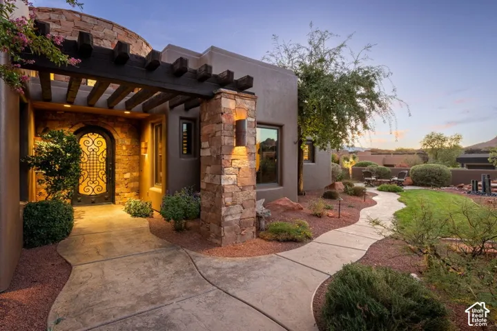 Stucco exterior with stone accents, a stone walkway, a decorative arched entry door, and a wooden pergola