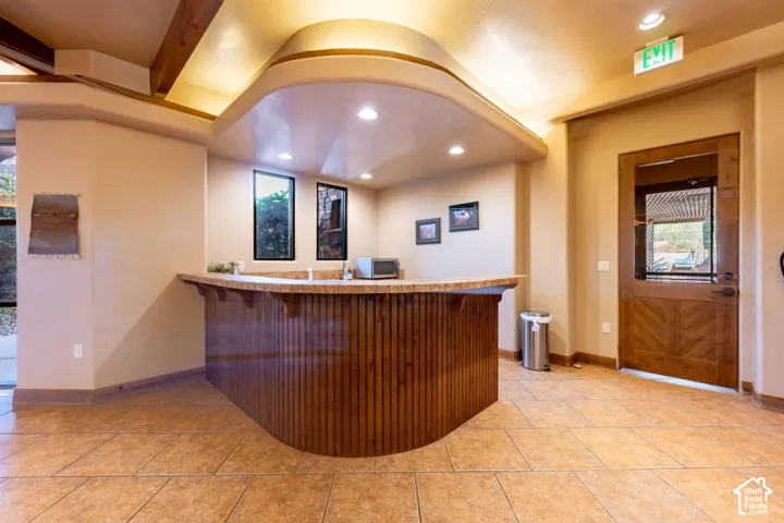 Built-in bar with wood-paneling and stone-finish countertop, ceramic tile flooring, recessed lighting, and exposed wood ceiling beams