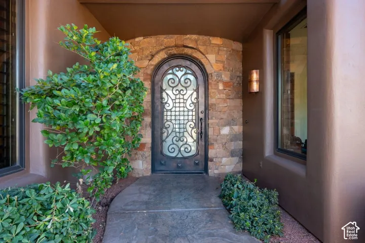 Arched entryway featuring an ornate wrought iron and glass door, stone surround, and stucco exterior