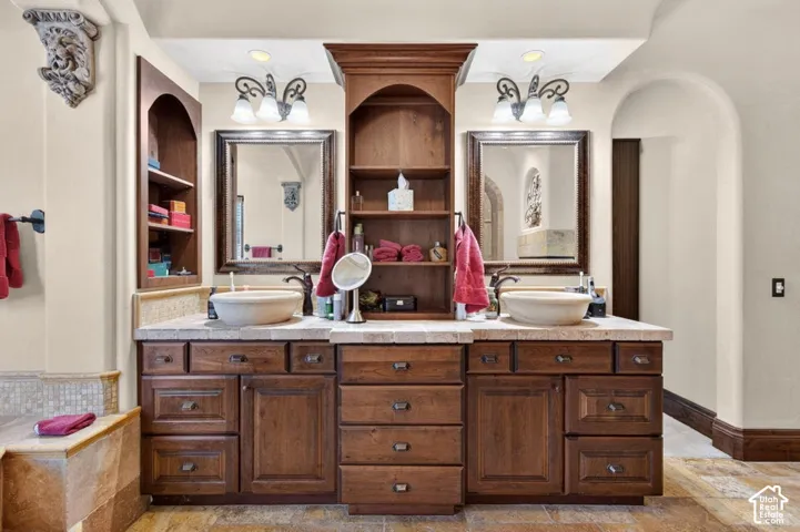 Dual vessel sinks, dark wood-finish cabinetry, built-in shelving, and complementary framed mirrors