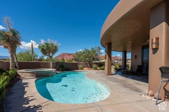 Curved outdoor pool with integrated spa, concrete decking, and an expansive covered patio featuring recessed lighting and wall sconces