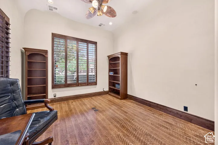 Wood-finish flooring, built-in shelving, wood window shutters, and a ceiling fan with integrated lighting