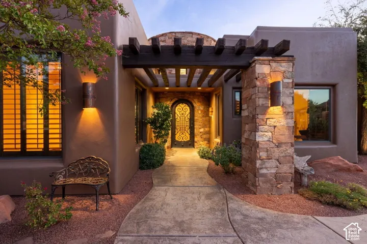 Stucco exterior with stone accents, a covered entry with a wooden pergola, an arched doorway with an ornate iron gate, and a concrete pathway