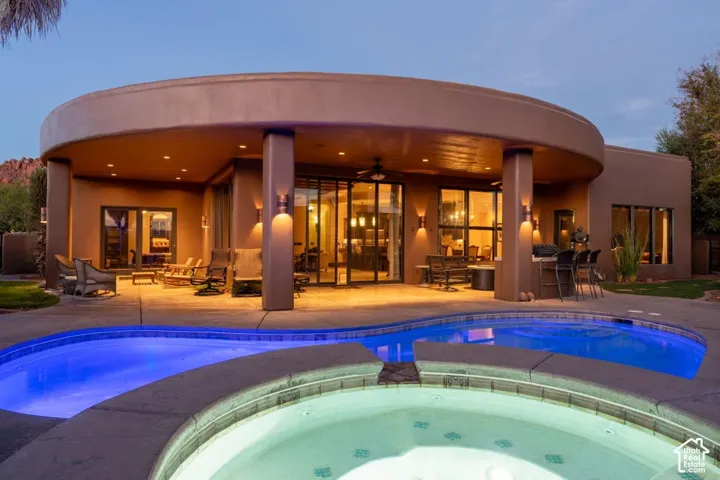 Curved stucco exterior with a covered patio, integrated outdoor bar, and a built-in swimming pool with an attached spa