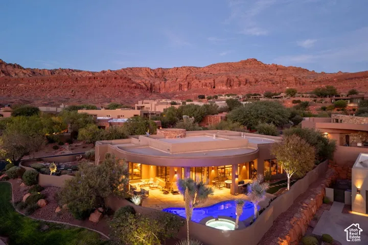 Curved stucco exterior with an integrated swimming pool, spa, and illuminated patio space