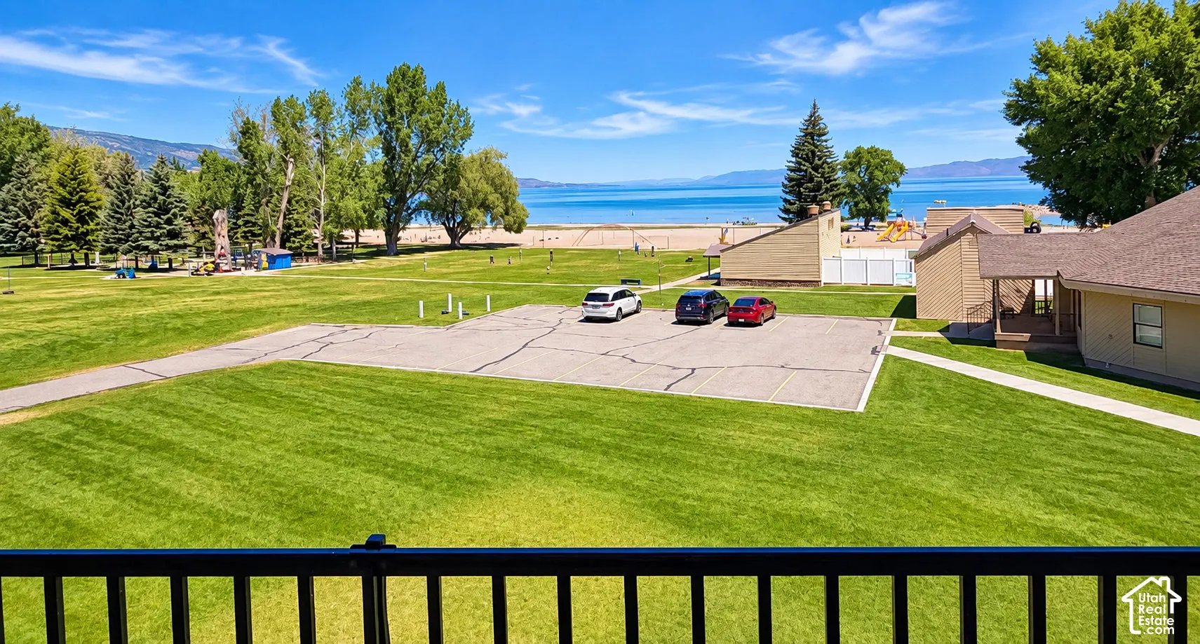Lush green lawn with paved pathways and a dedicated parking area, featuring mature trees and a distant body of water