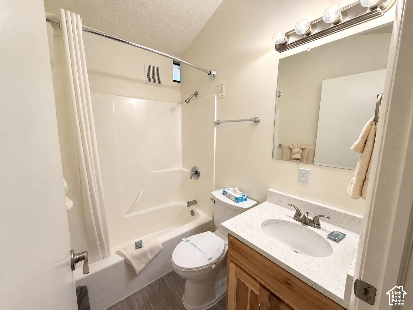 Bathroom featuring a shower-tub combination, vanity with a white countertop, wood-finish cabinetry, and a wall-mounted mirror with overhead lighting