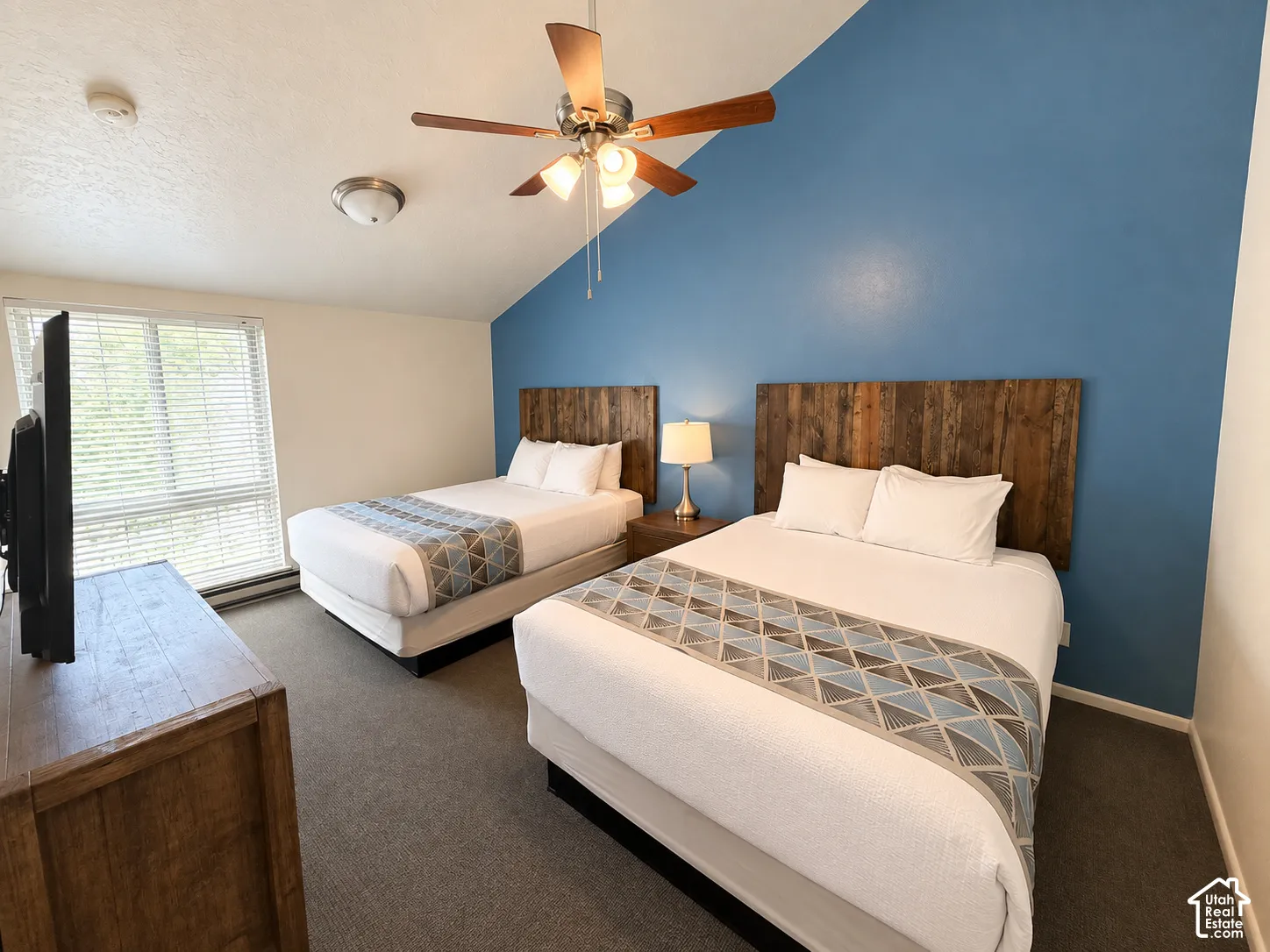 Vaulted ceiling with a ceiling fan, accent wall, wood-finish headboards, and a window with blinds