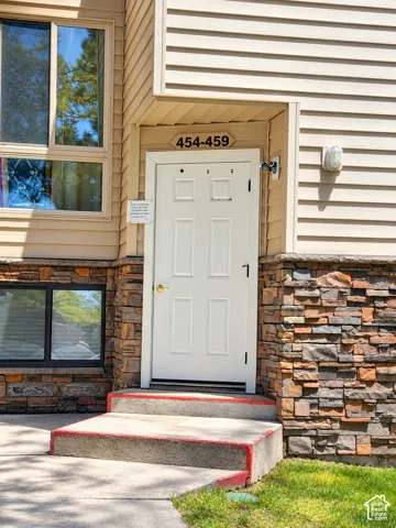 Multi-pane windows, light beige horizontal siding, stacked stone veneer facade, concrete entry steps, and a white paneled entry door